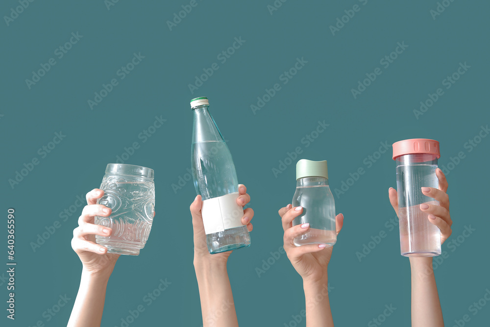 Female hands with bottles and glass of cold water on green background