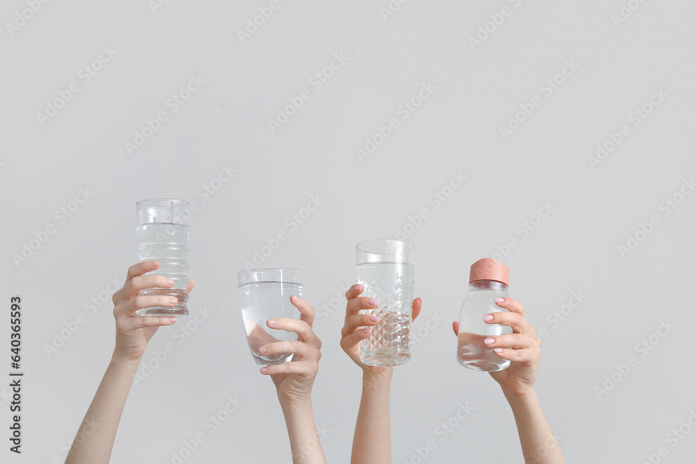 Female hands with bottle and glasses of cold water on light background