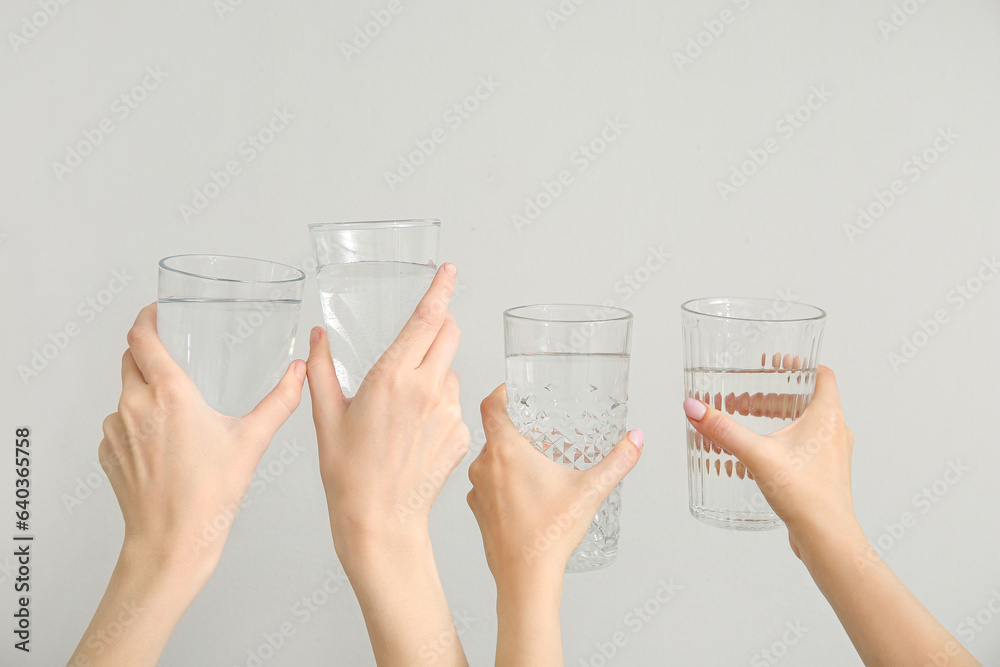 Female hands with glasses of cold water on light background