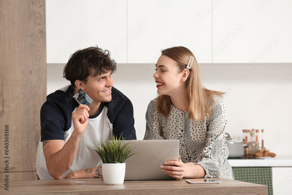 Young couple with laptop and gift card shopping online in kitchen