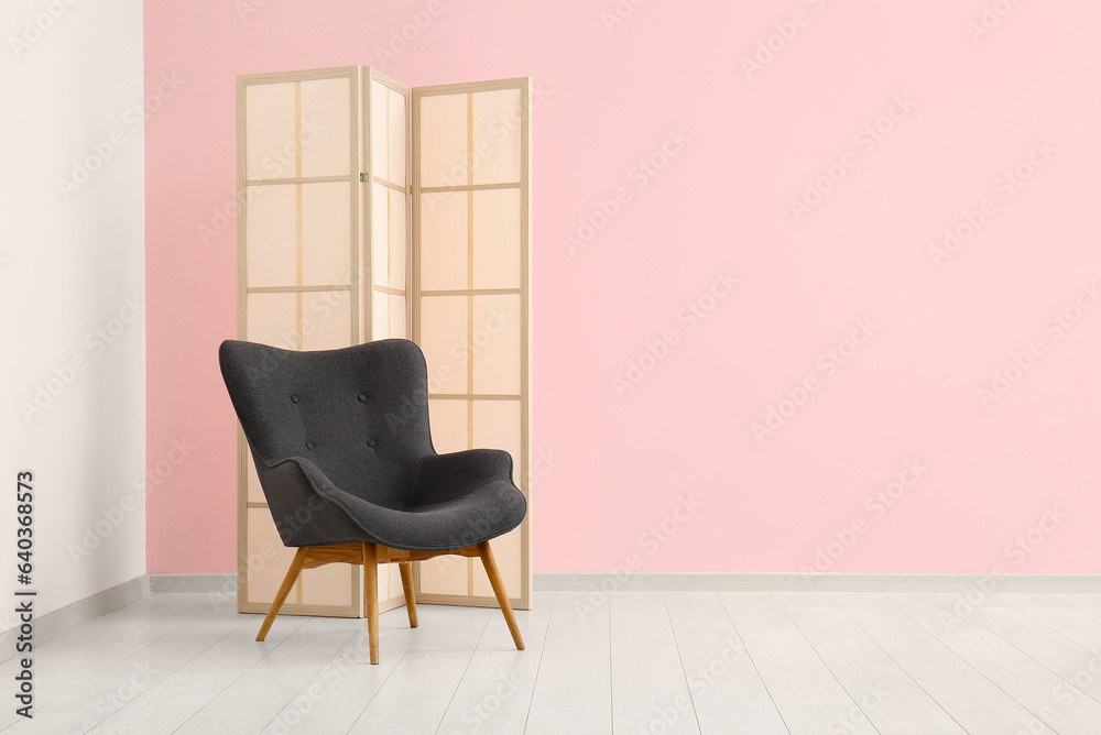 Grey armchair and folding screen near pink wall