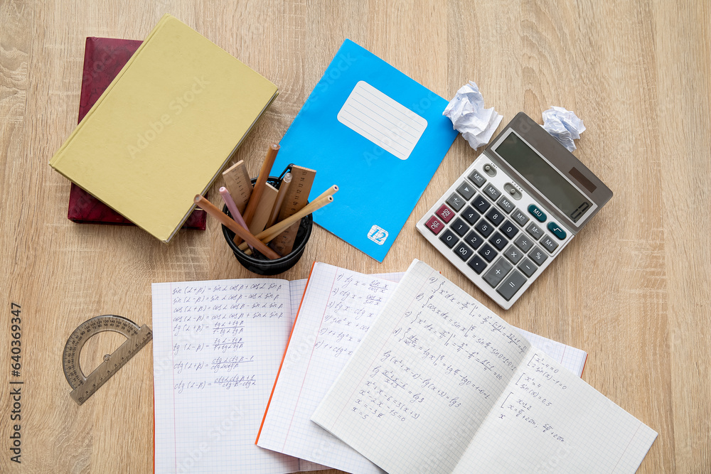 Open copybooks with math formulas and stationery on wooden table