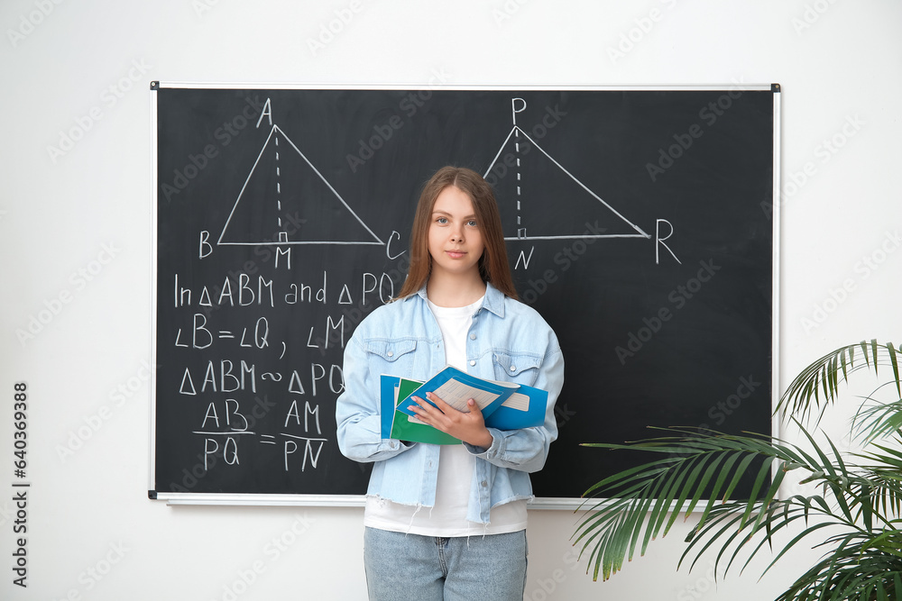 Young math teacher with copybooks near blackboard in classroom