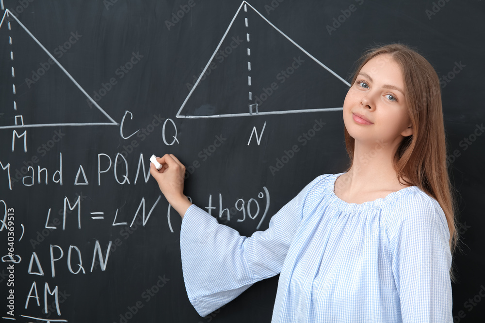 Young math teacher writing on blackboard in classroom