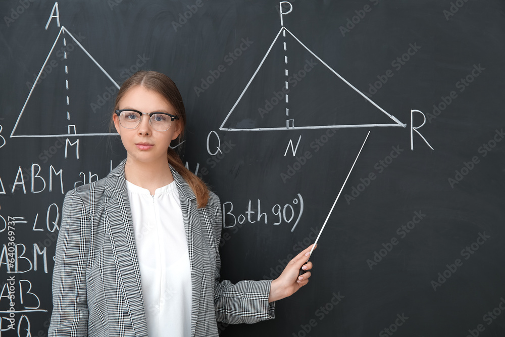 Young math teacher with pointer near blackboard in classroom