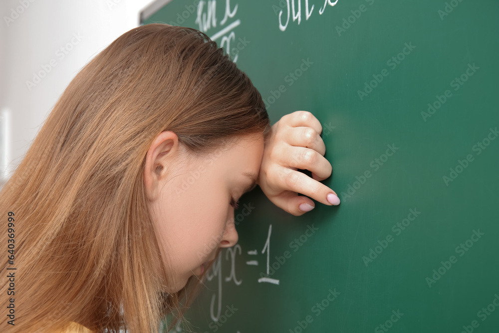 Tired young math teacher near blackboard in classroom, closeup