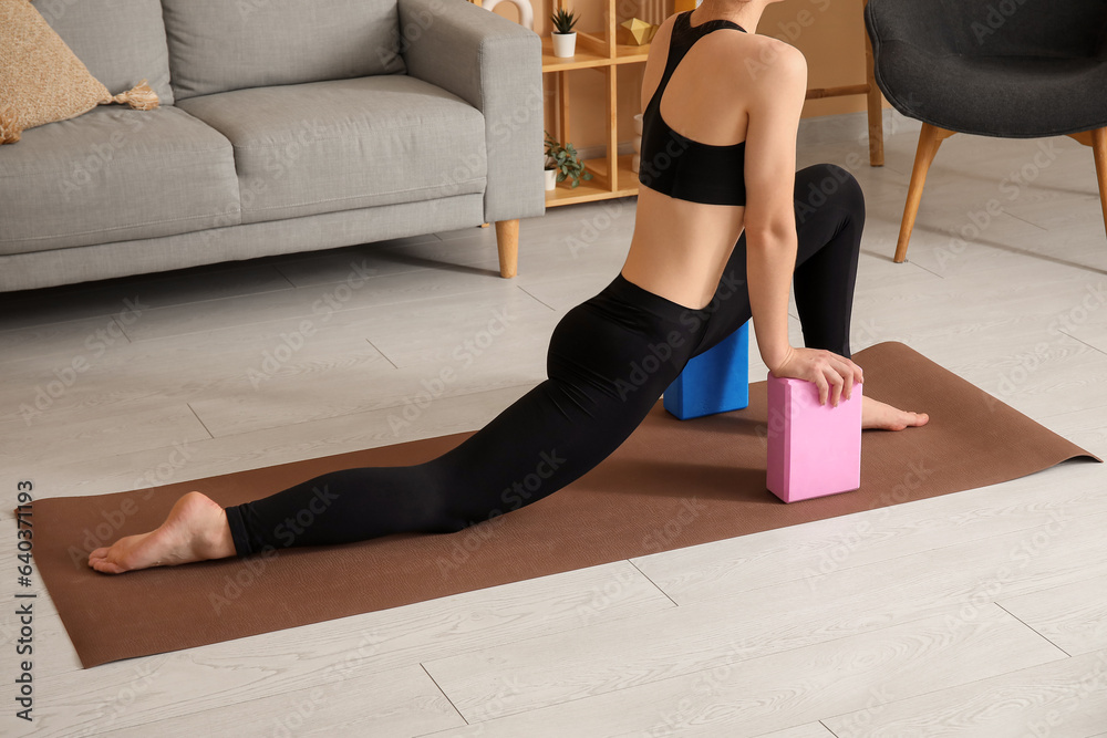 Sporty young woman practicing yoga with blocks at home