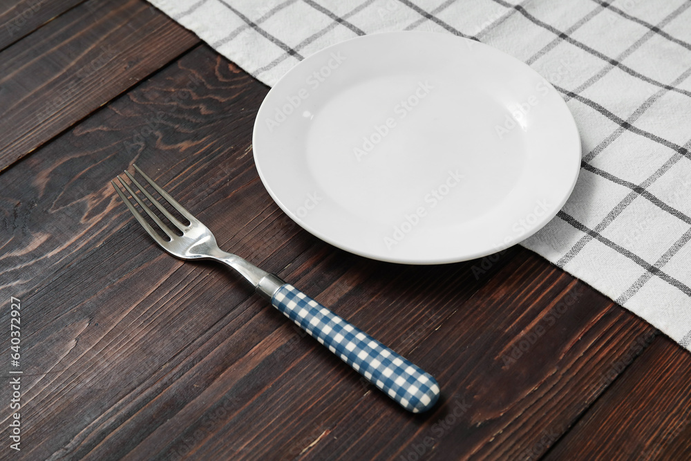 Clean plate, fork and napkin on wooden background