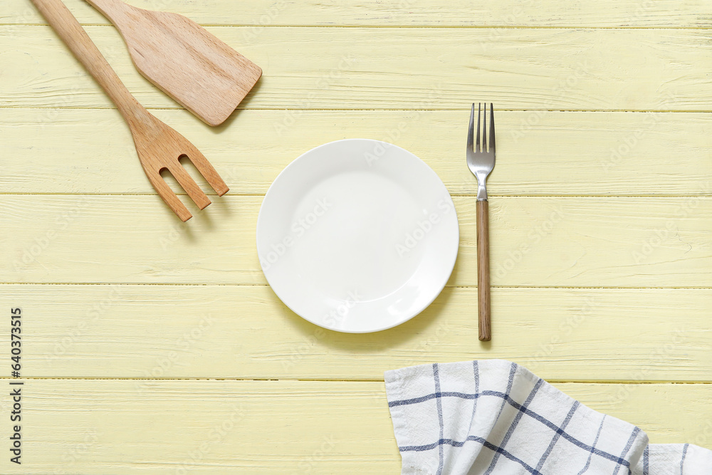 Clean plate, forks, spatula and napkin on yellow wooden background