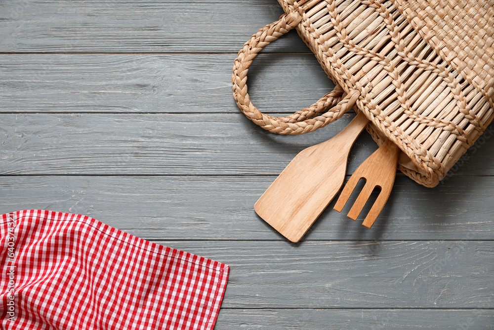 Wicker bag with fork, spatula and napkin on grey wooden background