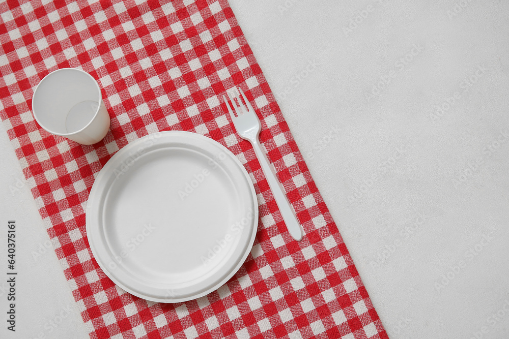 Disposable plate, cup, fork and napkin on light background