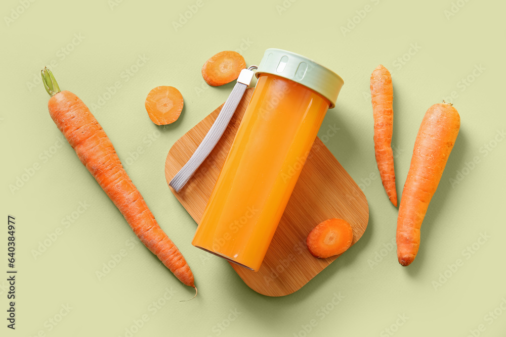 Wooden board with sports bottle of fresh carrot juice on green background