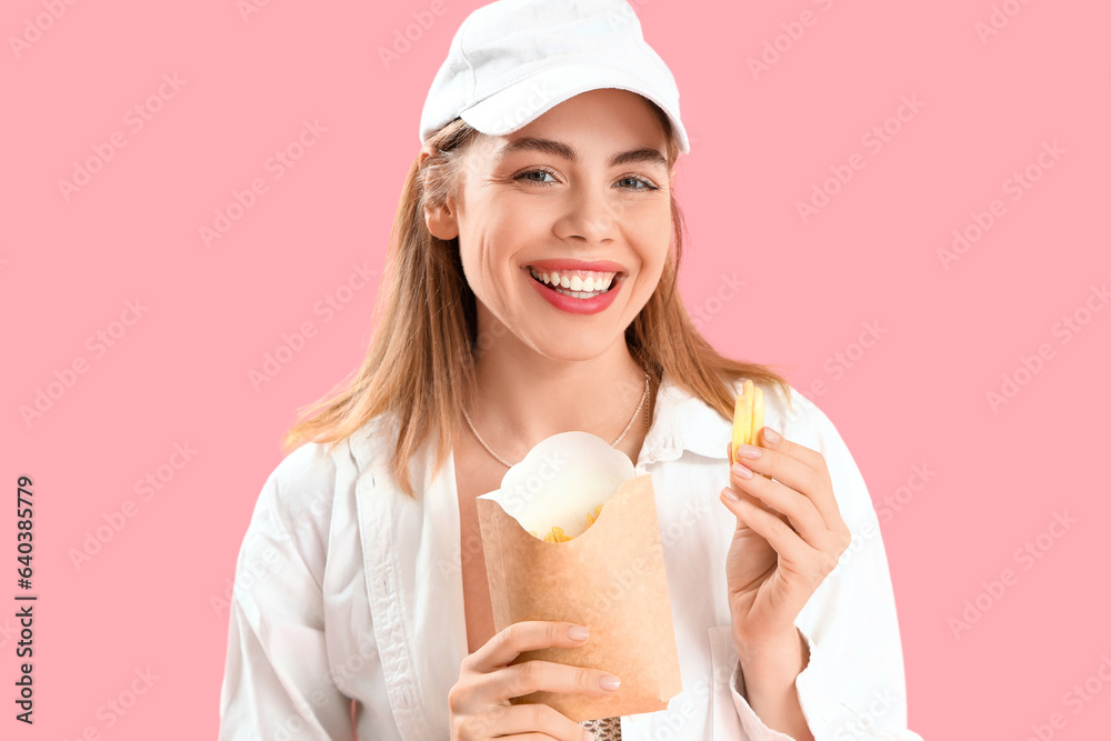 Beautiful happy young woman with pack of french fries on pink background