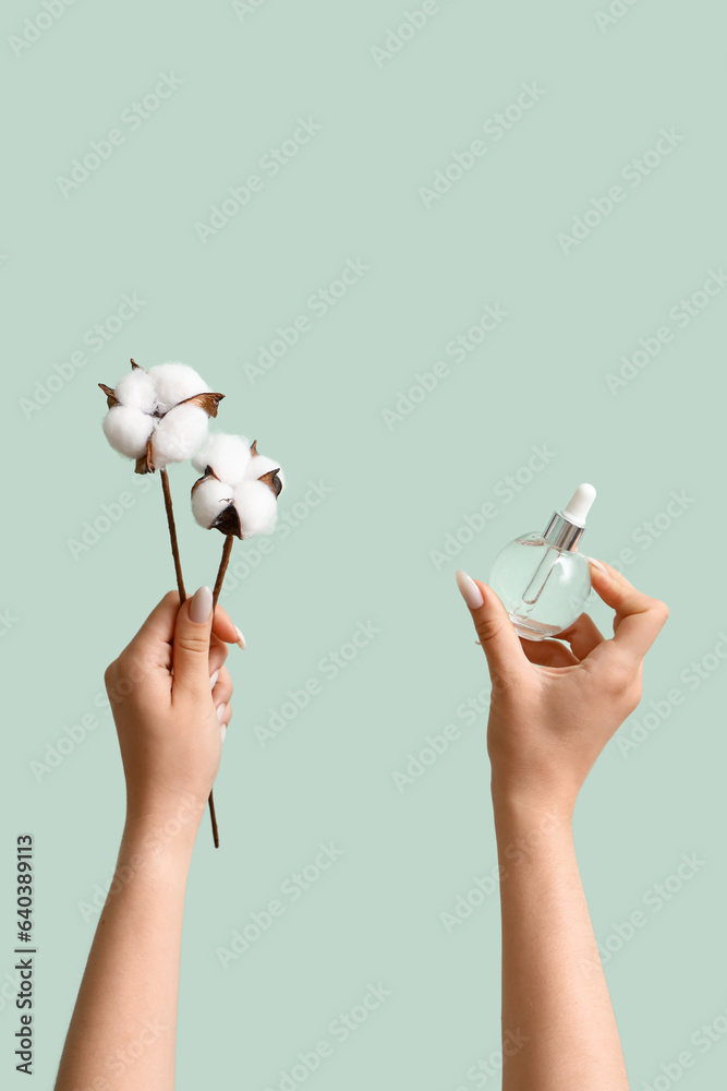 Woman with cosmetic dropper bottle and cotton flowers on green background