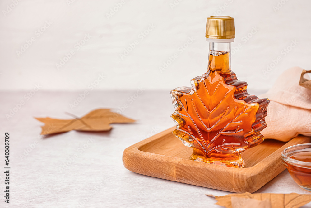 Bottle of tasty maple syrup on light background