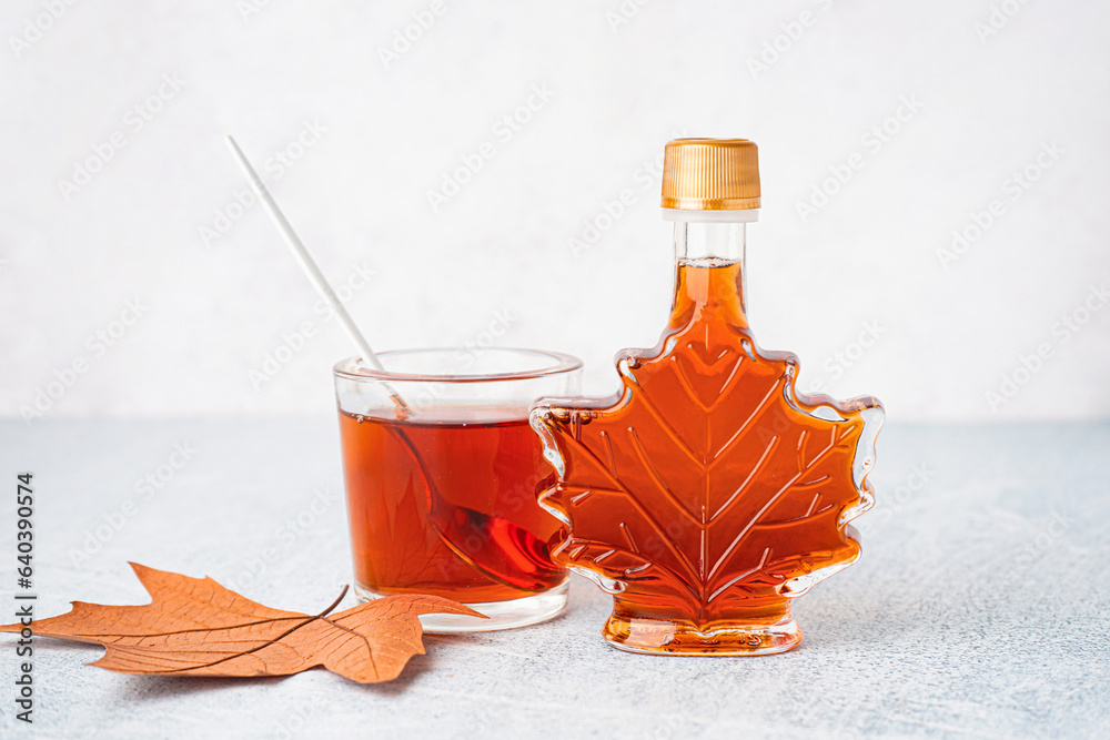 Bottle and glass of tasty maple syrup on table