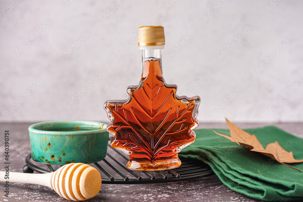 Bottle and bowl of tasty maple syrup on table