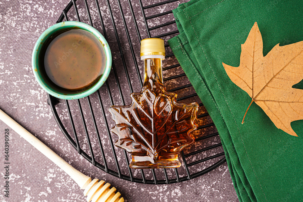 Bottle and bowl of tasty maple syrup on grey background