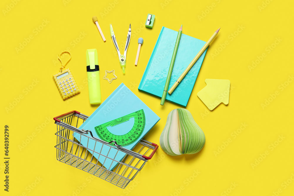 Composition with shopping basket and different stationery on yellow background