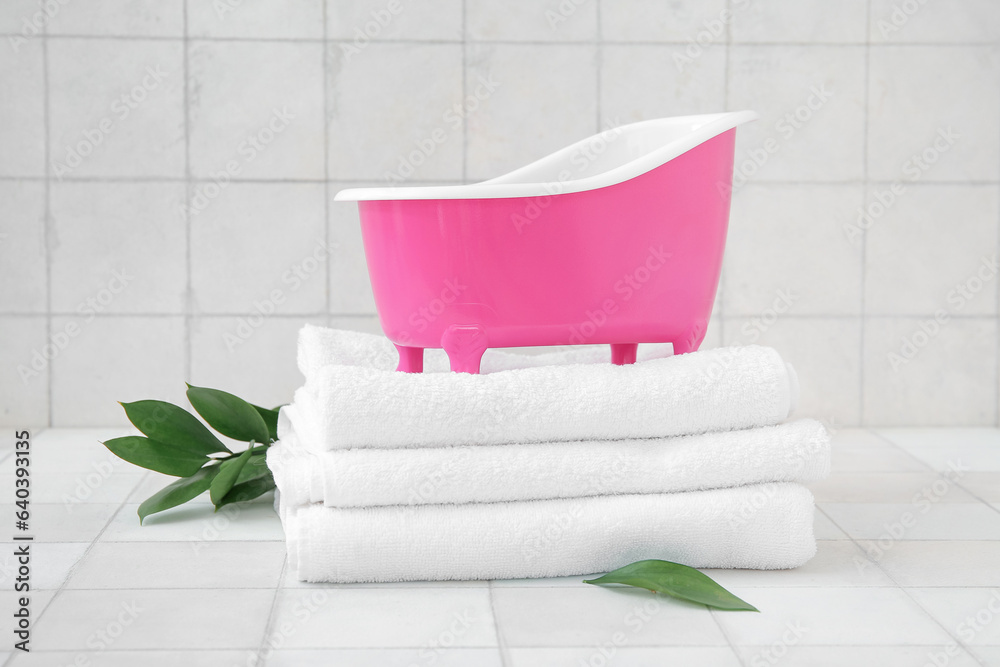 Small bathtub, clean towels and plant branch on light tile background