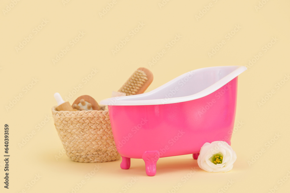 Small bathtub and basket with bath supplies on color background