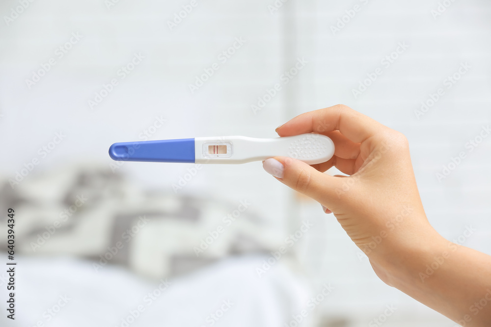 Female hand with positive pregnancy test on light background, closeup