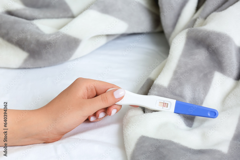 Female hand with positive pregnancy test and plaid on bed, closeup