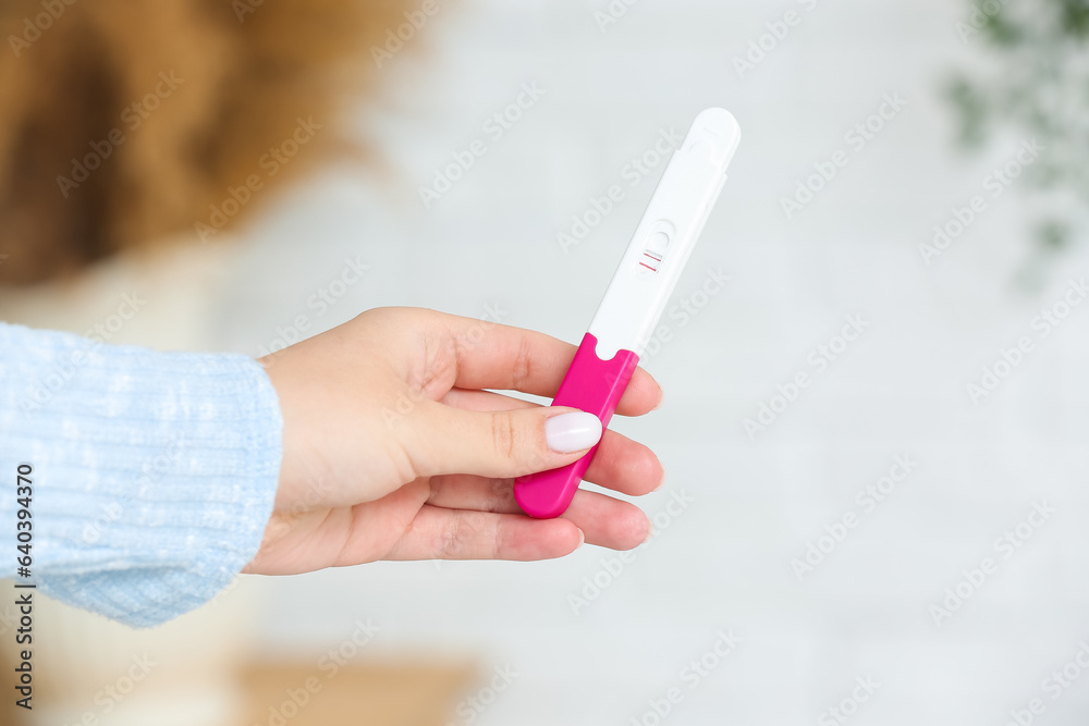 Female hand with positive pregnancy test on blurred background, closeup