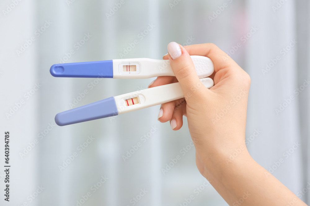 Female hand with positive pregnancy tests against window, closeup