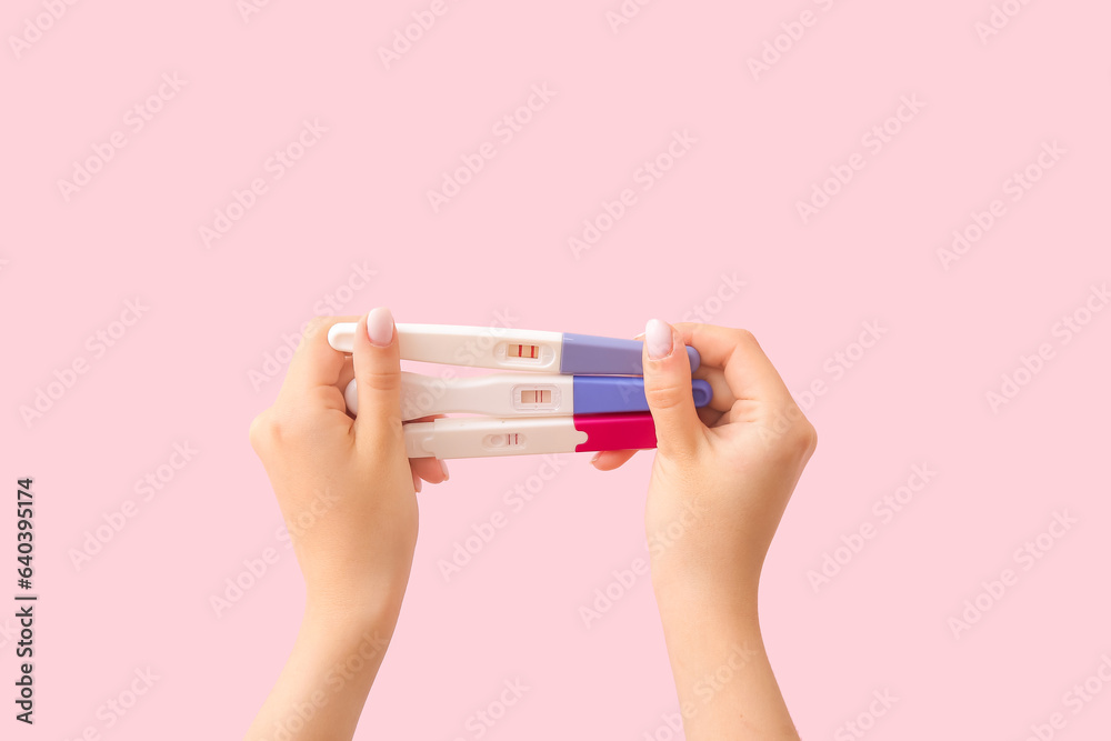 Female hands with different pregnancy tests on pink background