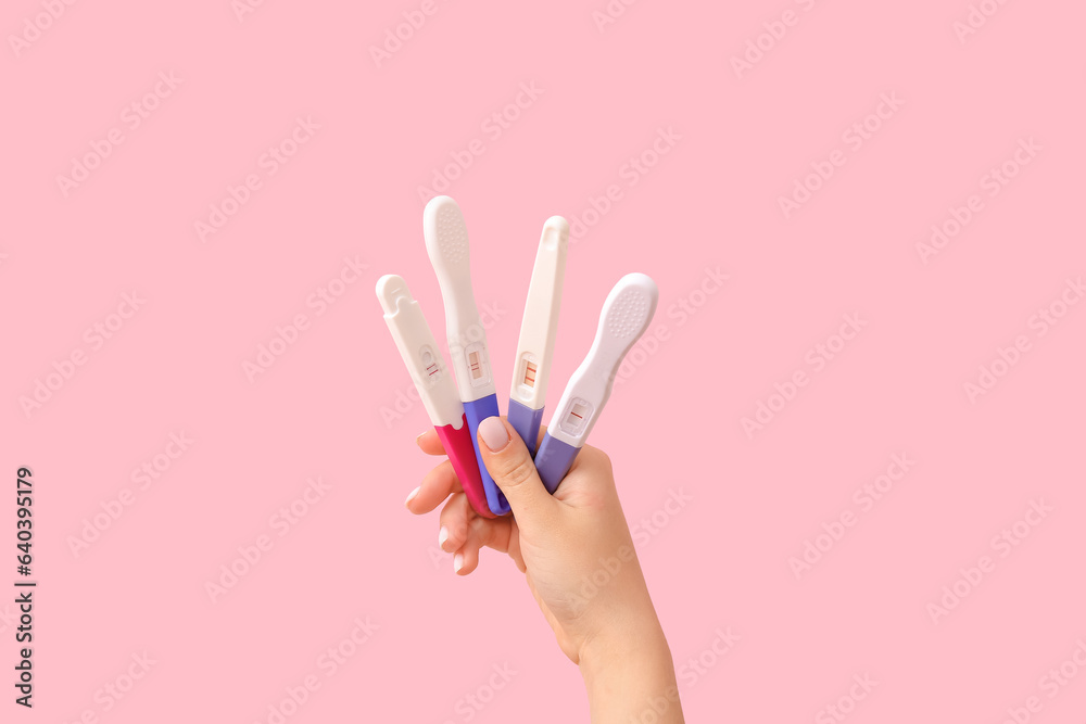 Female hand with different pregnancy tests on pink background