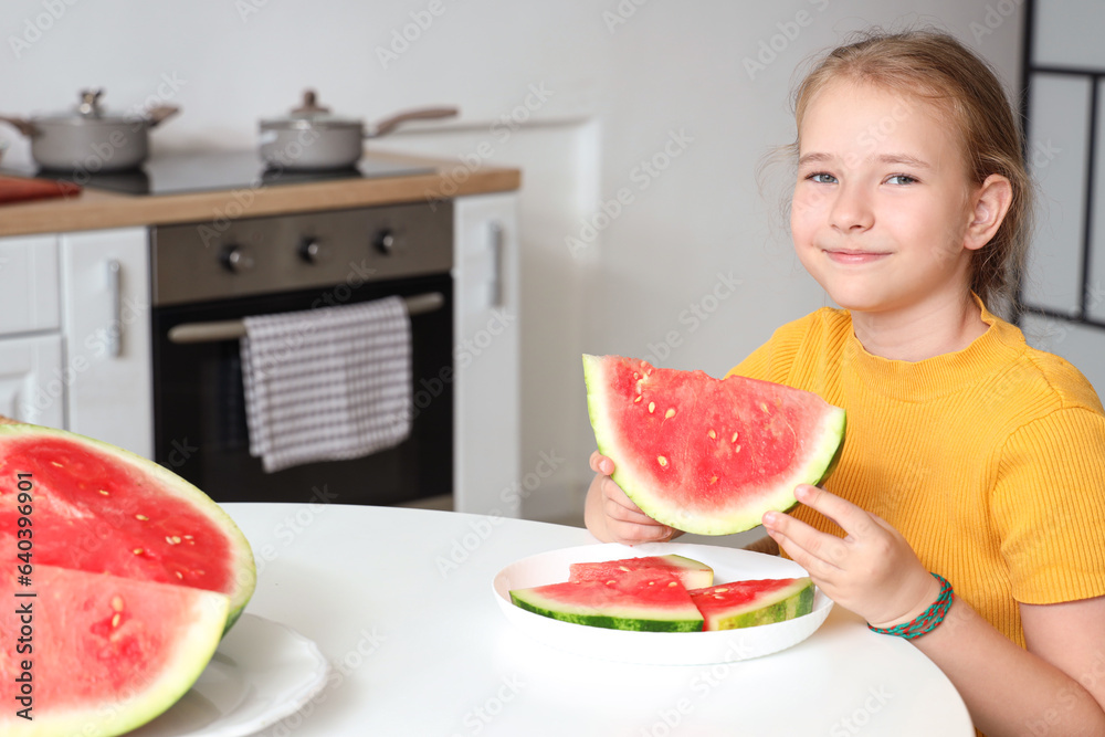 Happy little girl with slice of fresh watermelon sitting at table in kitchen