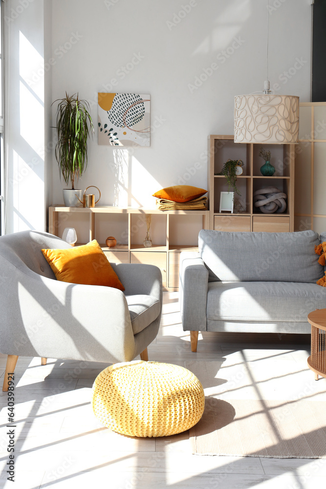 Interior of light living room with  grey sofa, armchair and pouf