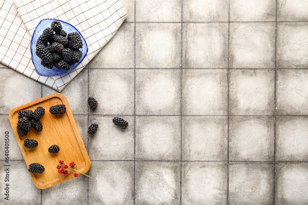 Wooden board and bowl with fresh blackberries on grey tile background