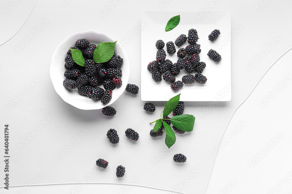 Plate and bowl with fresh blackberries on blue background