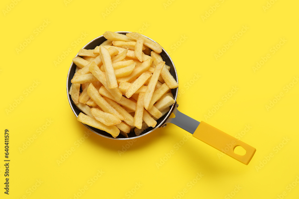 Golden french fries in frying pan on yellow background