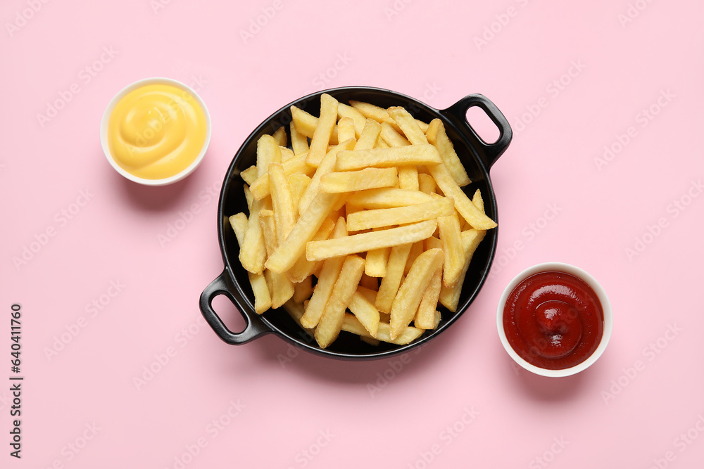 Black bowl with golden french fries, ketchup and cheese sauce on pink background