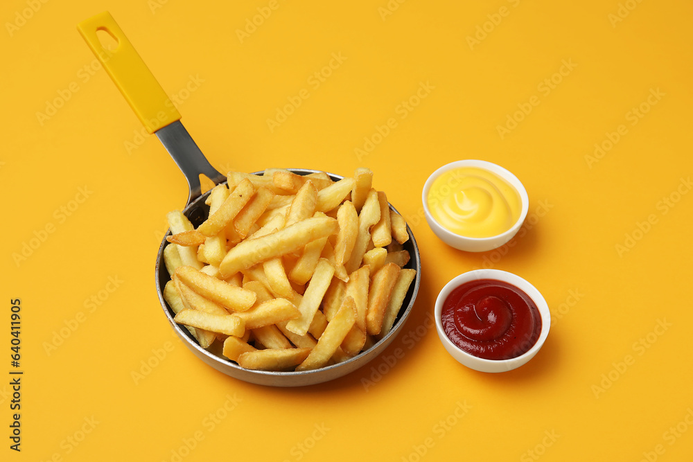 Frying pan with golden french fries, ketchup and cheese sauce on orange background