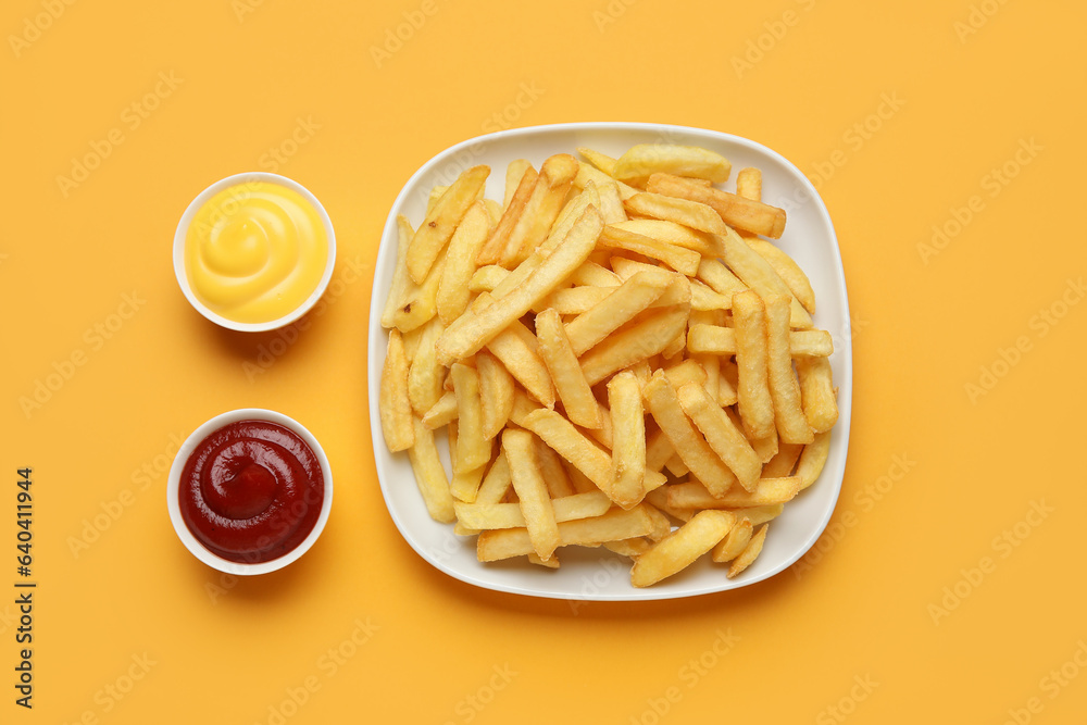 Plate with golden french fries, ketchup and cheese sauce on orange background