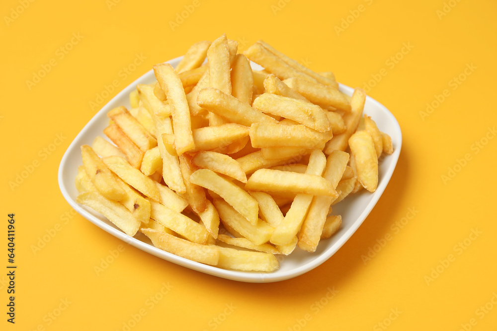 Plate with golden french fries on orange background