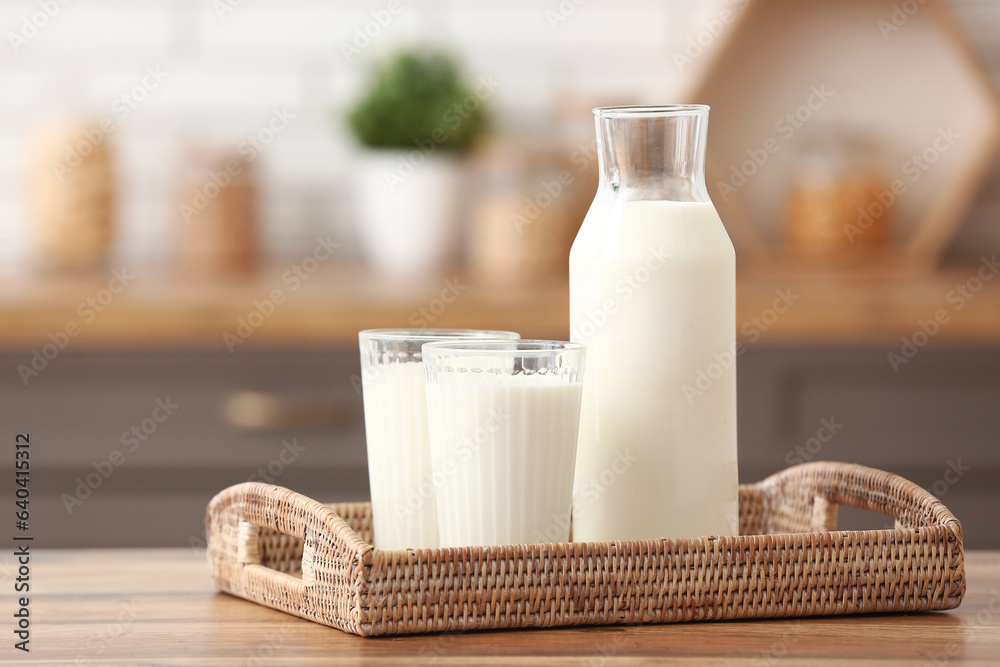 Glasses and bottle of fresh milk on wooden table in kitchen