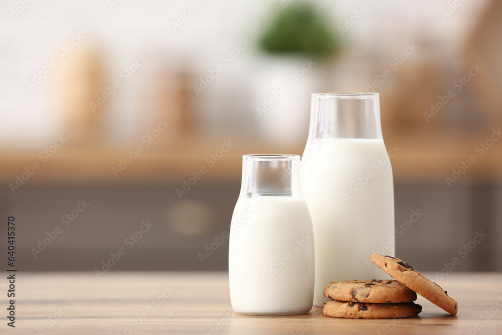 Bottles of fresh milk with sweet cookies on wooden table in kitchen