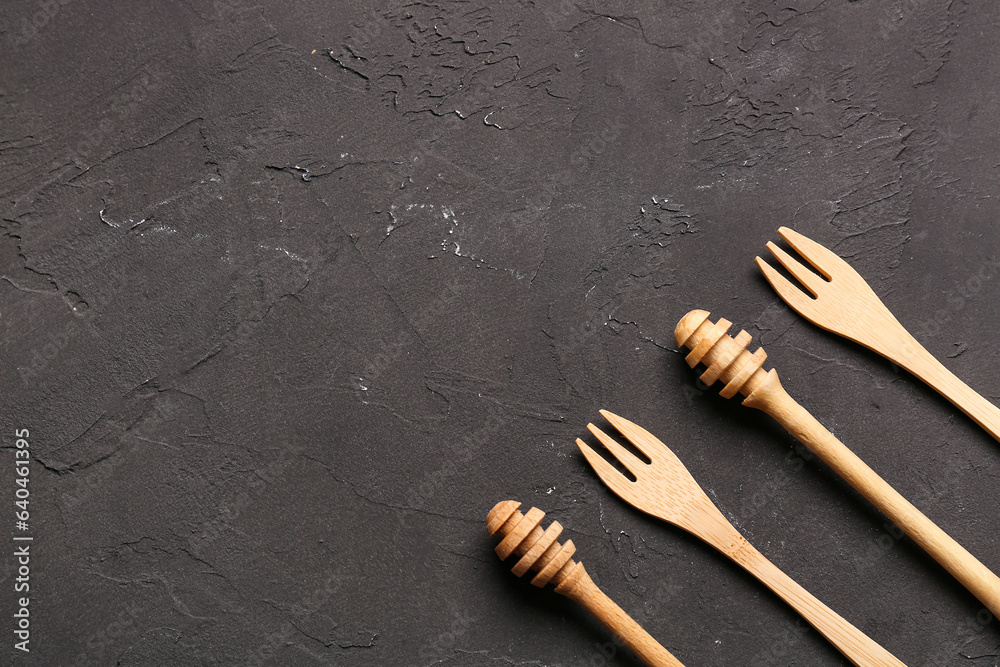 Wooden honey dippers and forks on black background