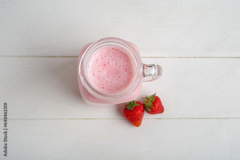 Mason jar of tasty strawberry smoothie on light wooden background