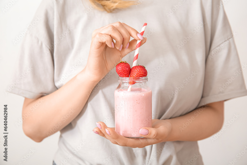 Woman holding mason jar of tasty strawberry smoothie on light background