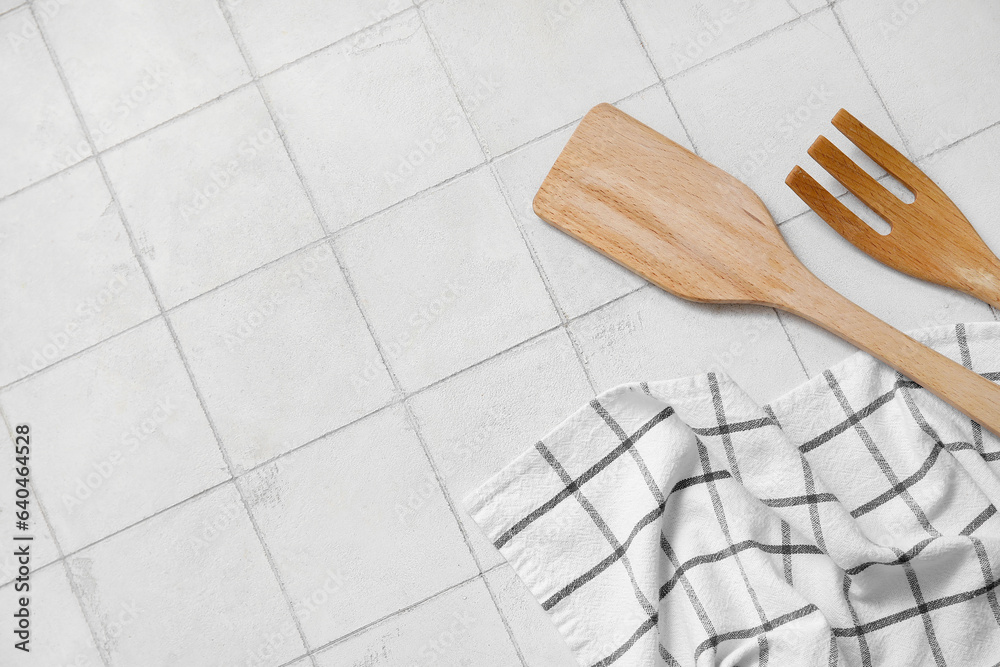 Wooden spatula, fork and napkin on white tile background