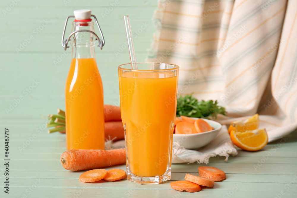 Glass and bottle of fresh carrot juice with orange on green wooden table