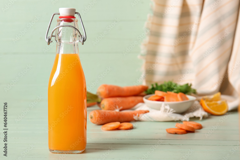 Bottle of fresh carrot juice with orange on green wooden table