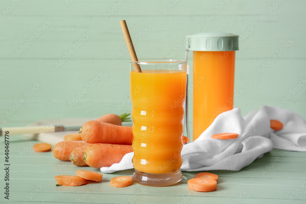 Glass and sports bottle of fresh carrot juice on green wooden table