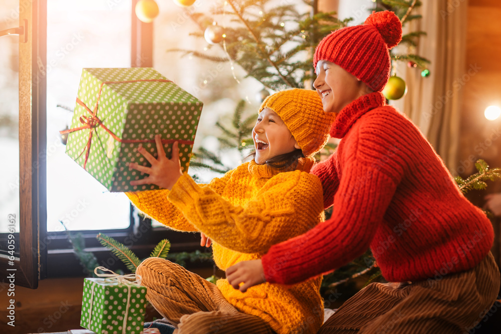 Happy children open gift boxes near the Christmas tree. Wonderful snowy winter background. Family ce